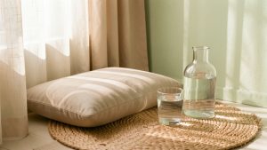 Coin de méditation lumineux avec coussin neutre, verre d’eau à température ambiante et bouteille en verre dans une ambiance douce et naturelle.